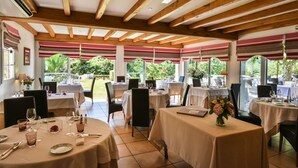 A restaurant with round tables, wooden beams, and large windows overlooking a garden. - Jardins de Bakea (Biriatou)
