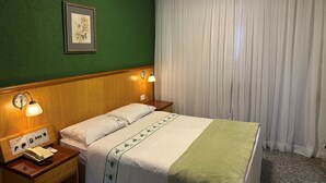 Habitación de hotel con cama, mesita de noche con teléfono, lámpara de pared e imagen enmarco.
