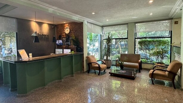 A reception area with a counter, seating, and large windows. - Hotel Pantanal Chácara Klabin (São Paulo)