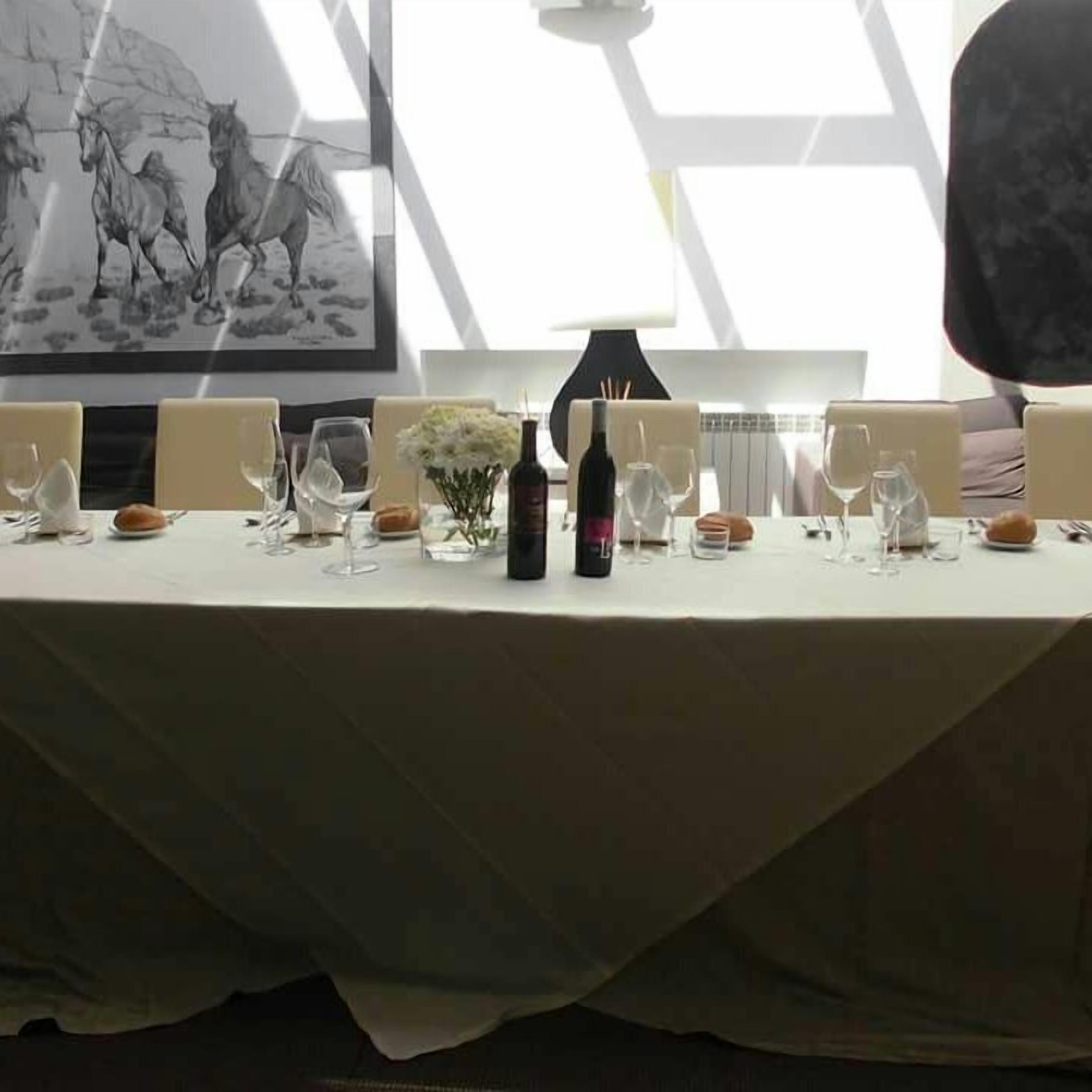 Una mesa de comedor lista con copas de vino, una botella y un jarrón con flores.