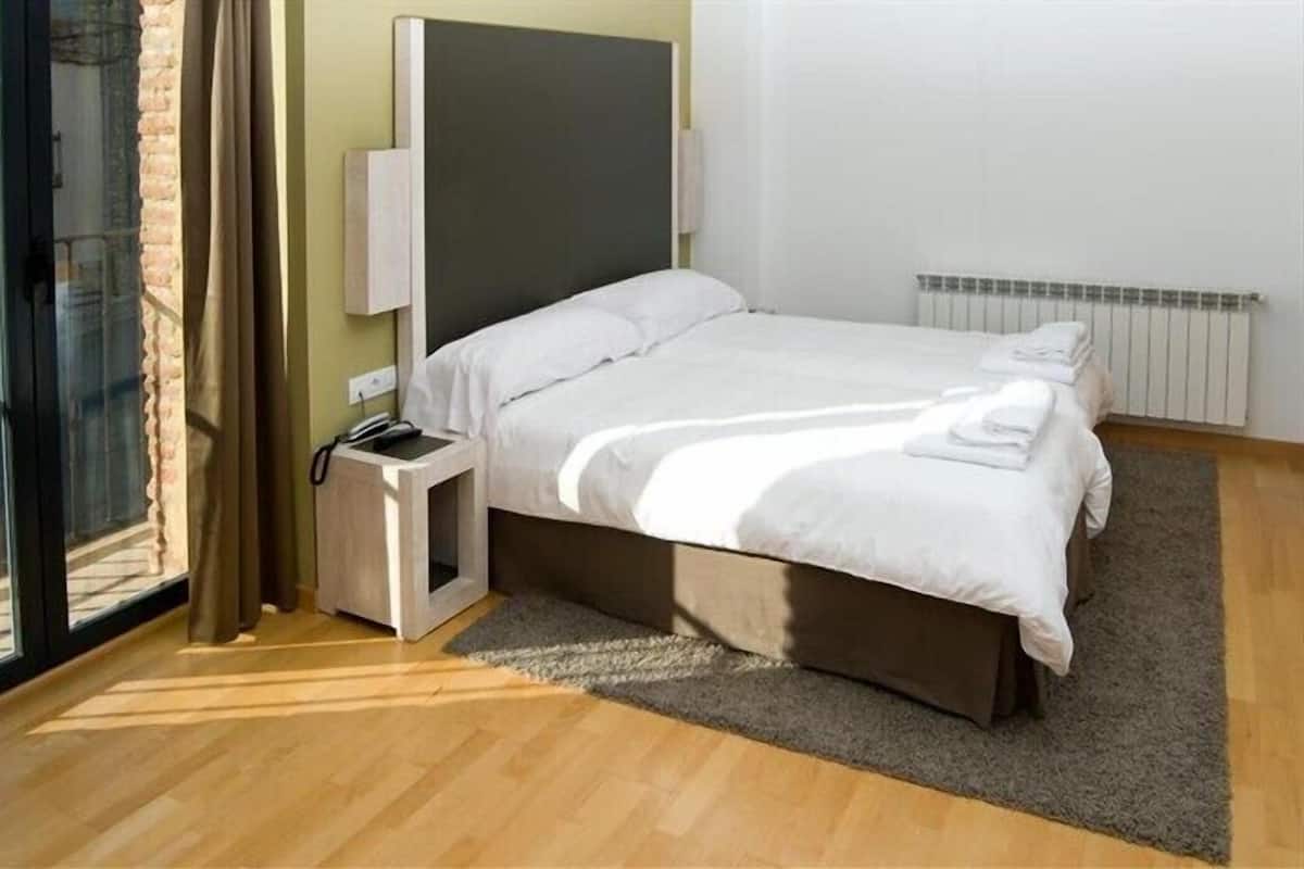 A bedroom with a bed, bedside table, and a view of the outdoors.