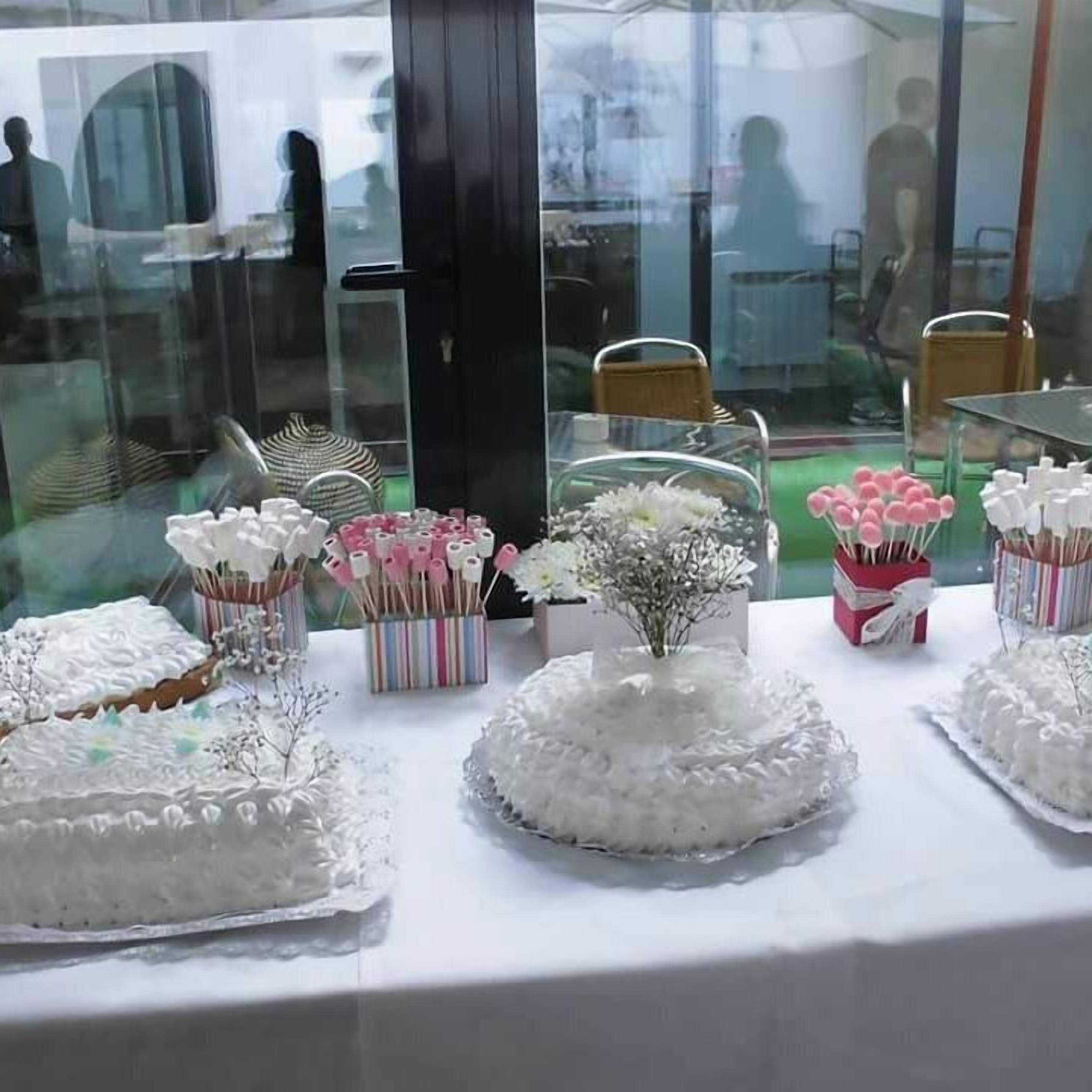 Een tafel met diverse taarten en decoraties, waaronder een taart met witte glazuur decoraties en een bloemstuk.