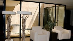 A modern interior with white sofas, two tall floor lamps, and a large window with a view of a staircase. - Hospedium Hotel Convento Santa Ana (Atienza)