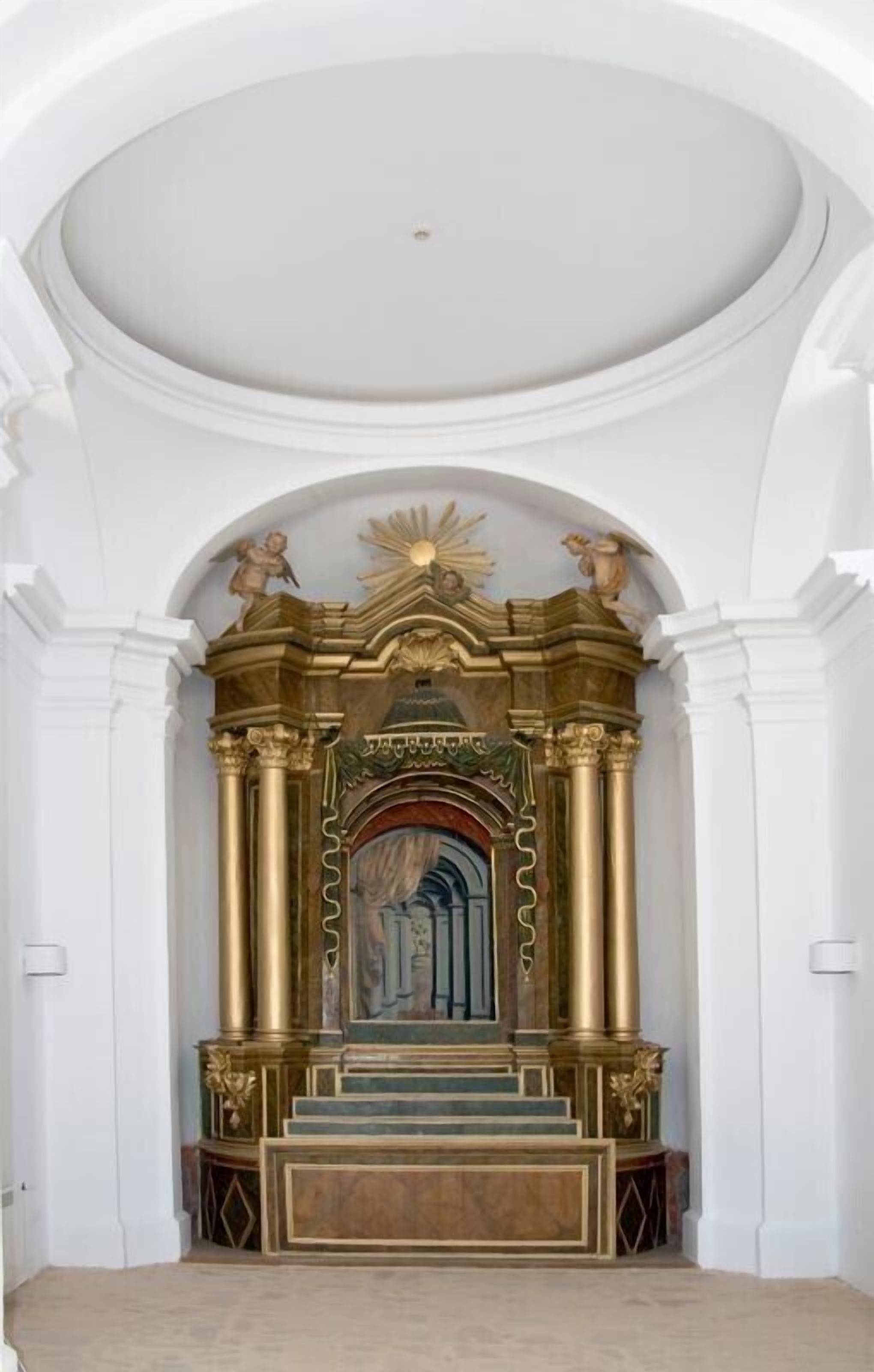 A grand, ornate altar with a golden frame, a statue of an angel, and a sun motif above it.