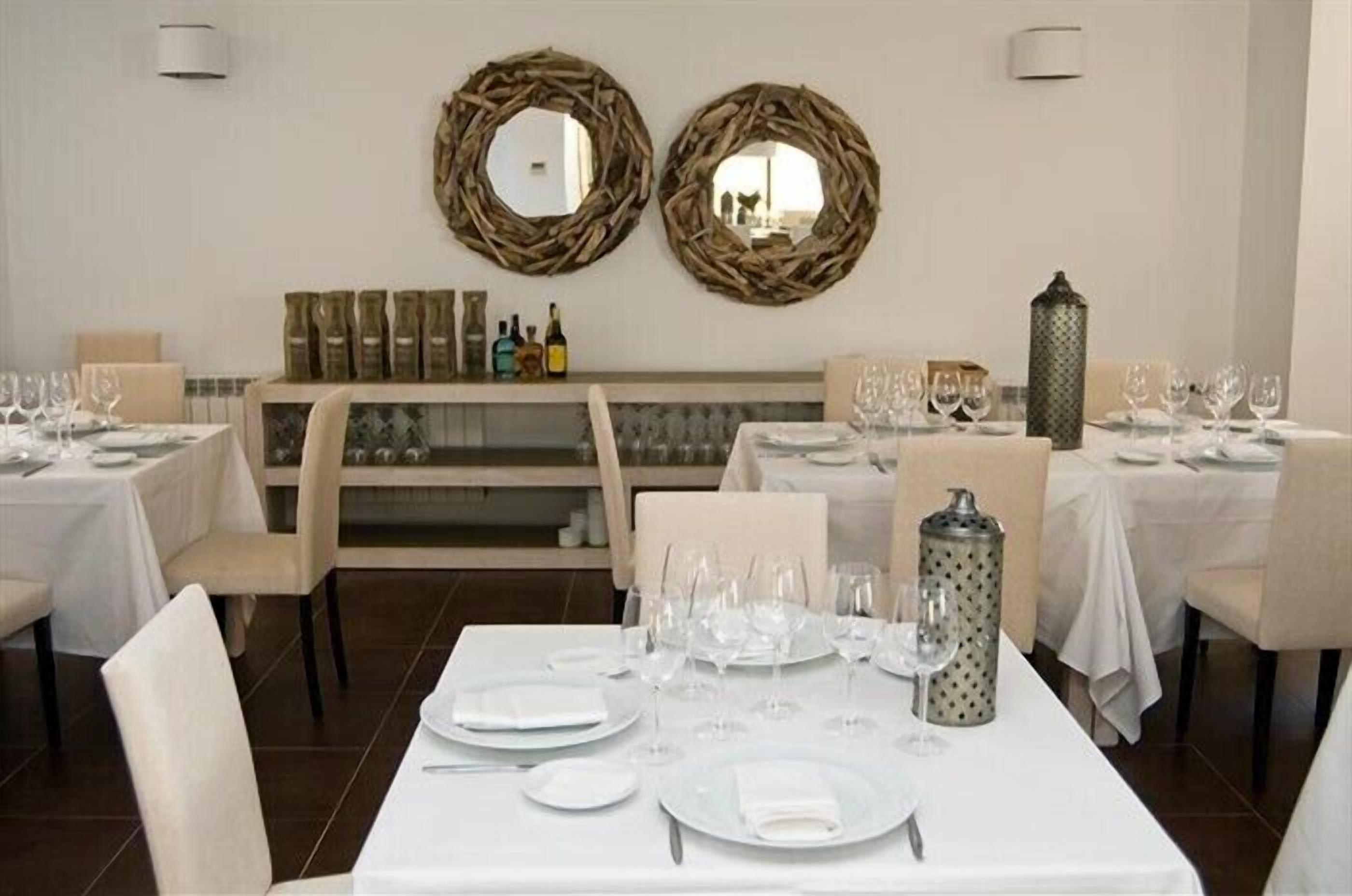 Un restaurant où les tables sont dressées pour le service, avec une décoration intérieure aux couleurs neutres et des éléments décoratifs en osier sur les murs.