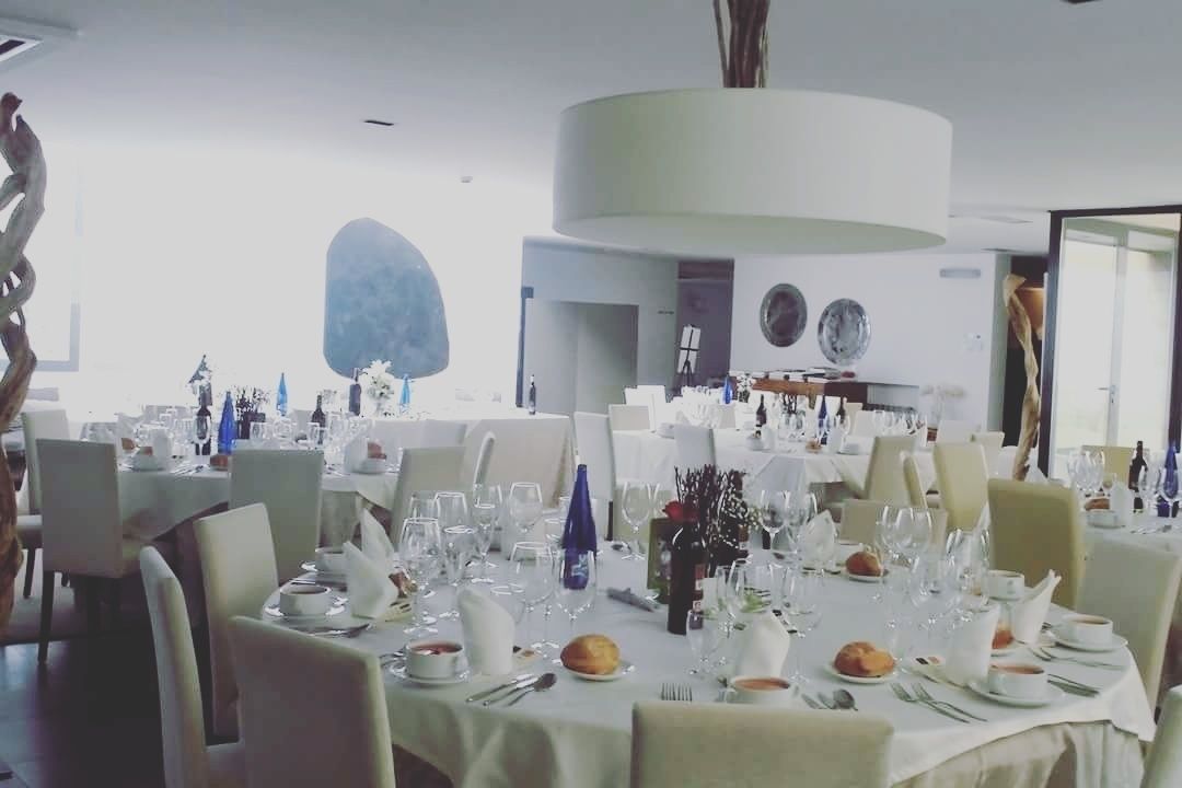 Un comedor con mesas redondas dispuestas para una comida, con manteles blancos, platos y cubiertos.
