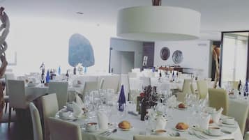 Un comedor con mesas redondas dispuestas para una comida, con manteles blancos, platos y cubiertos.