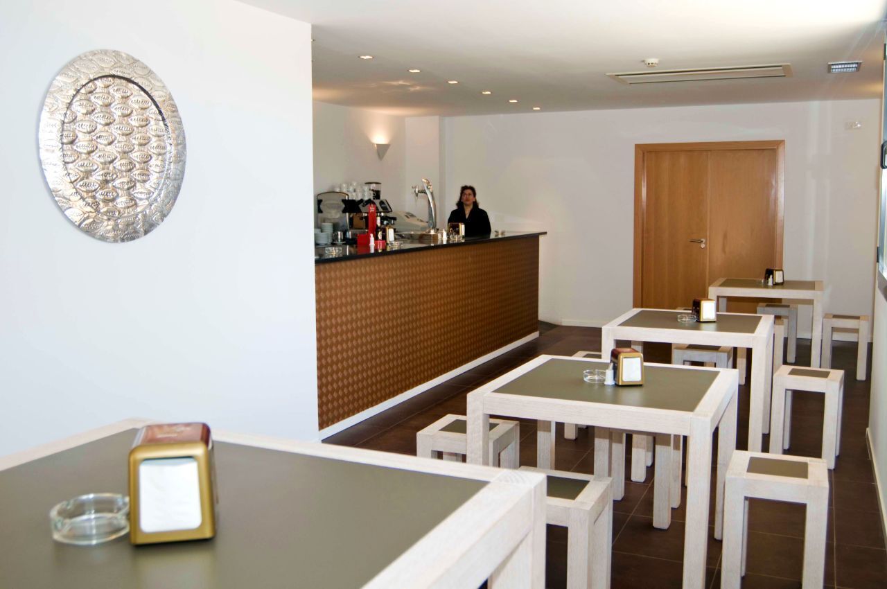 A hotel lobby with a reception desk, a coffee machine, and several tables and chairs.