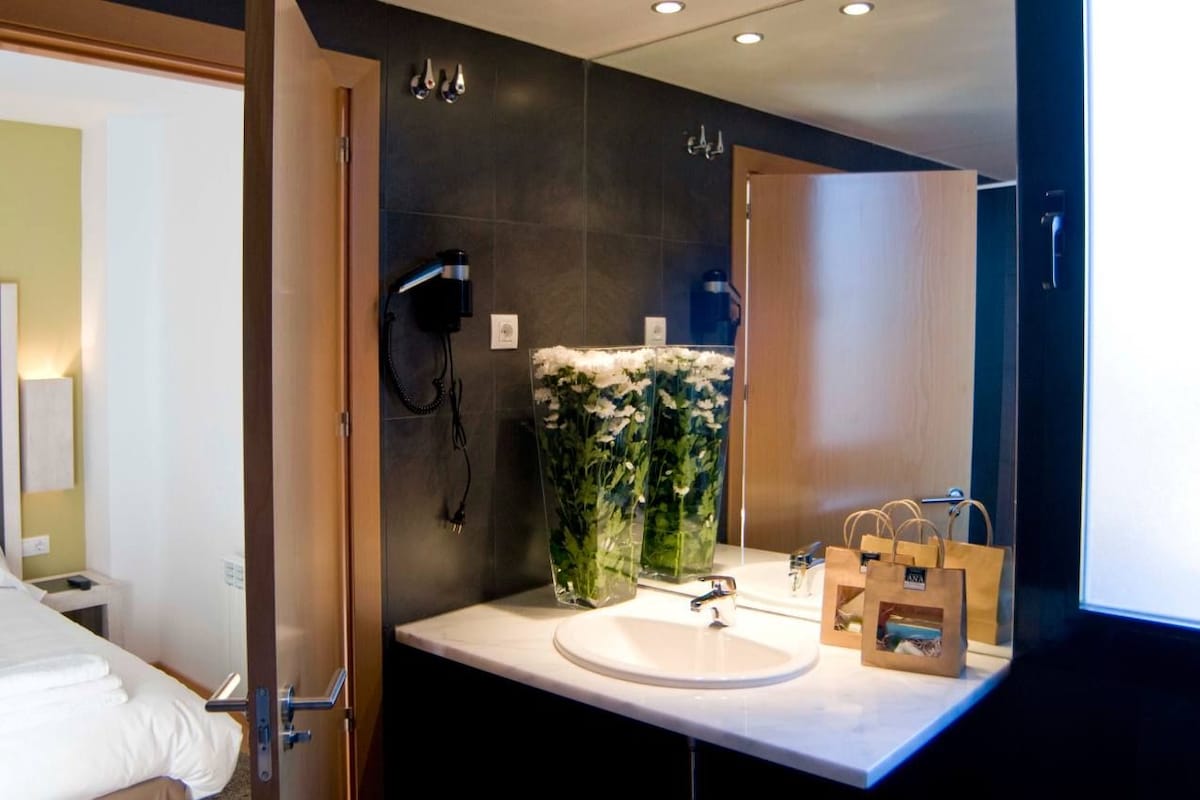 A modern bathroom with a large mirror, a white sink, and a vase of white flowers.