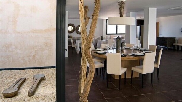 A modern dining area with a round table set for four, surrounded by chairs. A unique wooden sculpture stands in the foreground. - Hospedium Hotel Convento Santa Ana (Atienza)