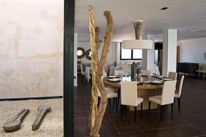 A modern dining area with a round table set for four, surrounded by chairs. A unique wooden sculpture stands in the foreground. - Hospedium Hotel Convento Santa Ana (Atienza)