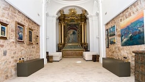 A spacious lobby with a stone wall, framed artwork, and a central decorative area with steps leading to a golden altar. - Hospedium Hotel Convento Santa Ana (Atienza)