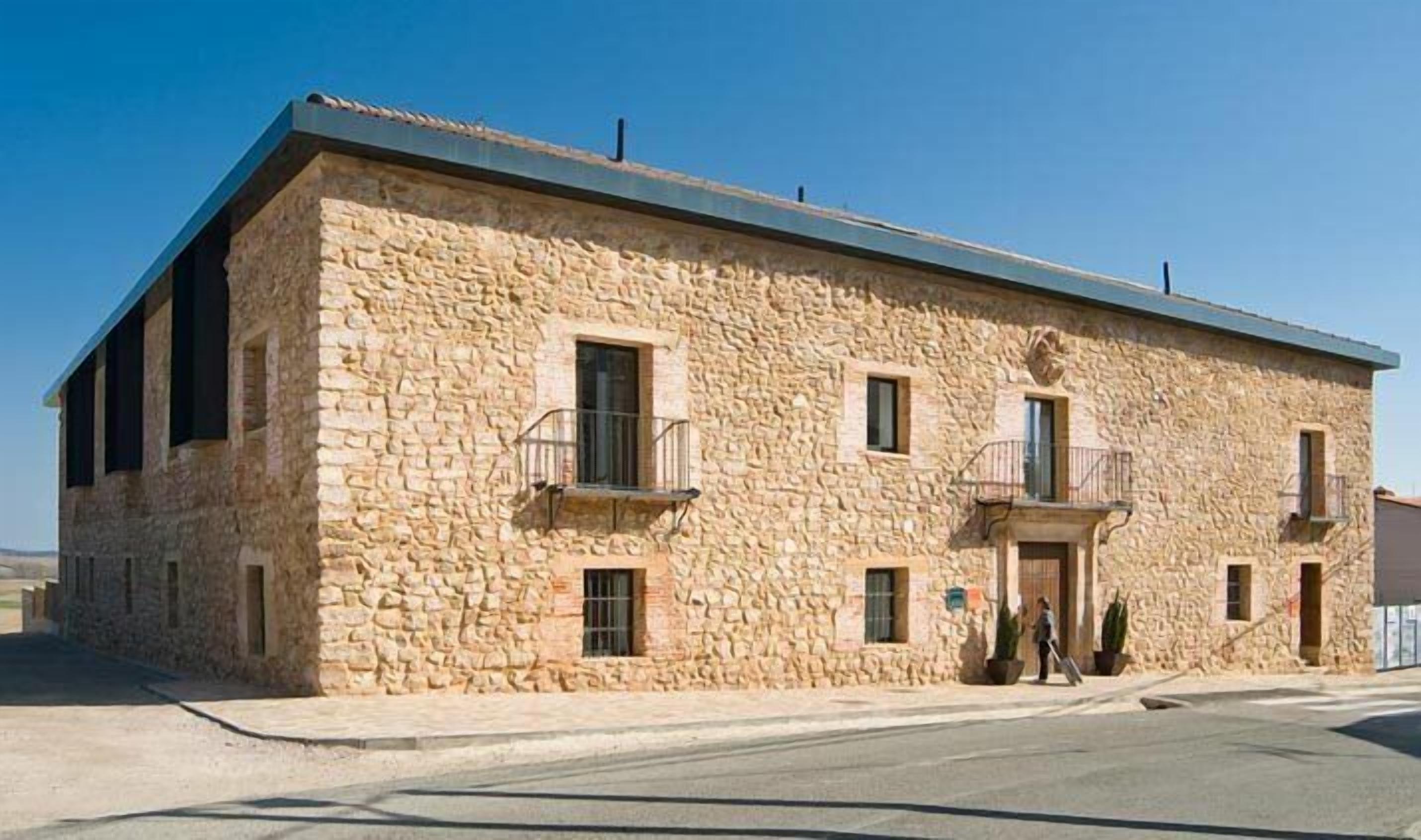 A stone building with a flat roof, two balconies, and a small entrance.