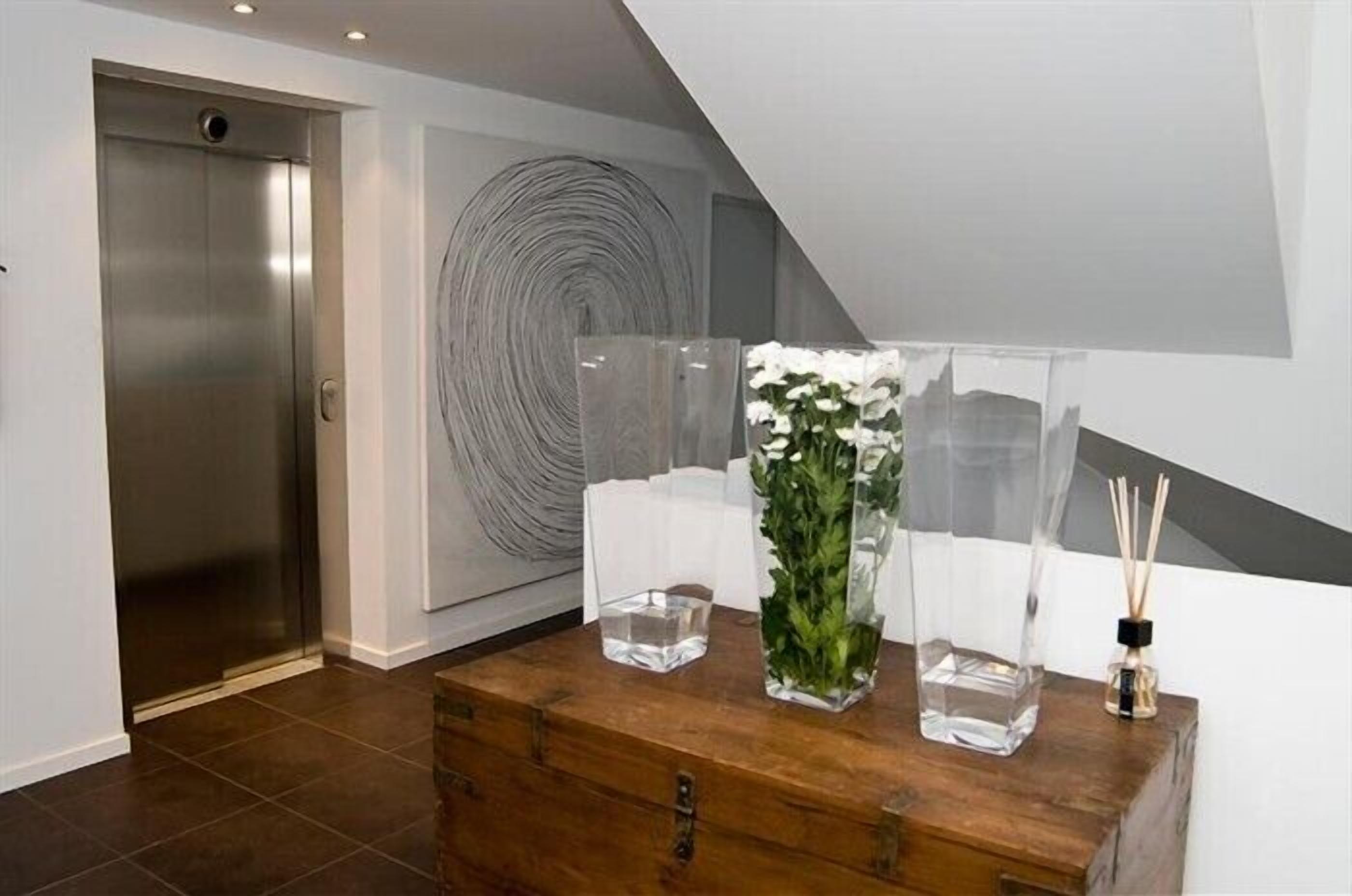 Un interior moderno con un cofre de madera, jarrones de vidrio transparente con flores y una gran obra de arte abstracto en la pared.