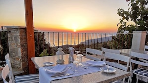 Ein Tisch für zwei Personen mit Blick auf den Sonnenuntergang über dem Meer, weiße Stühle und eine Steinsäule.