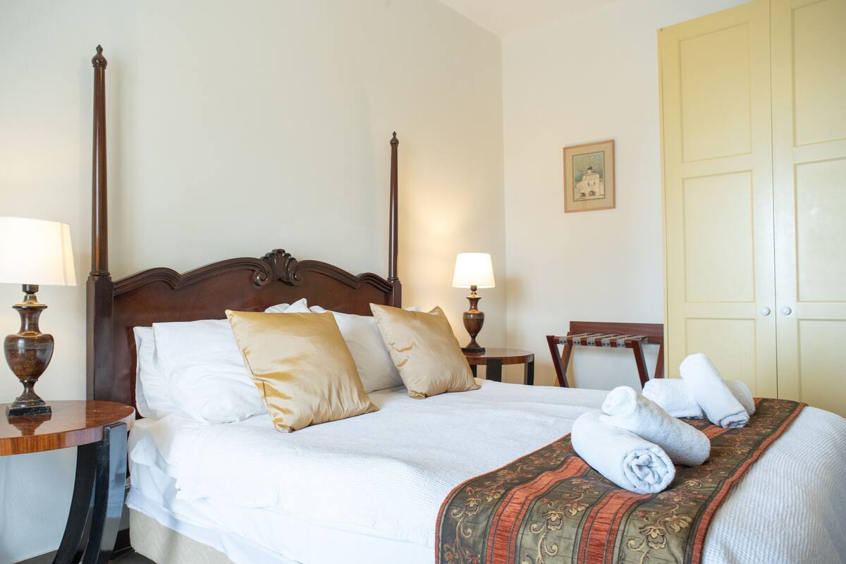 A neatly made bed with white linens and a patterned throw blanket, two bedside lamps, and a wooden nightstand with a lamp.