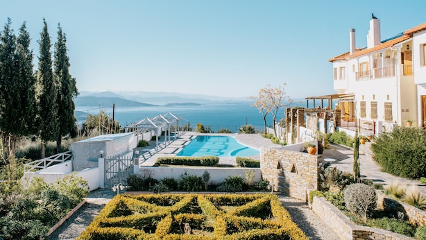 Ein Poolbereich mit Blick auf das Meer, umgeben von viel Grün und einem weißen Gebäude mit Balkonen.