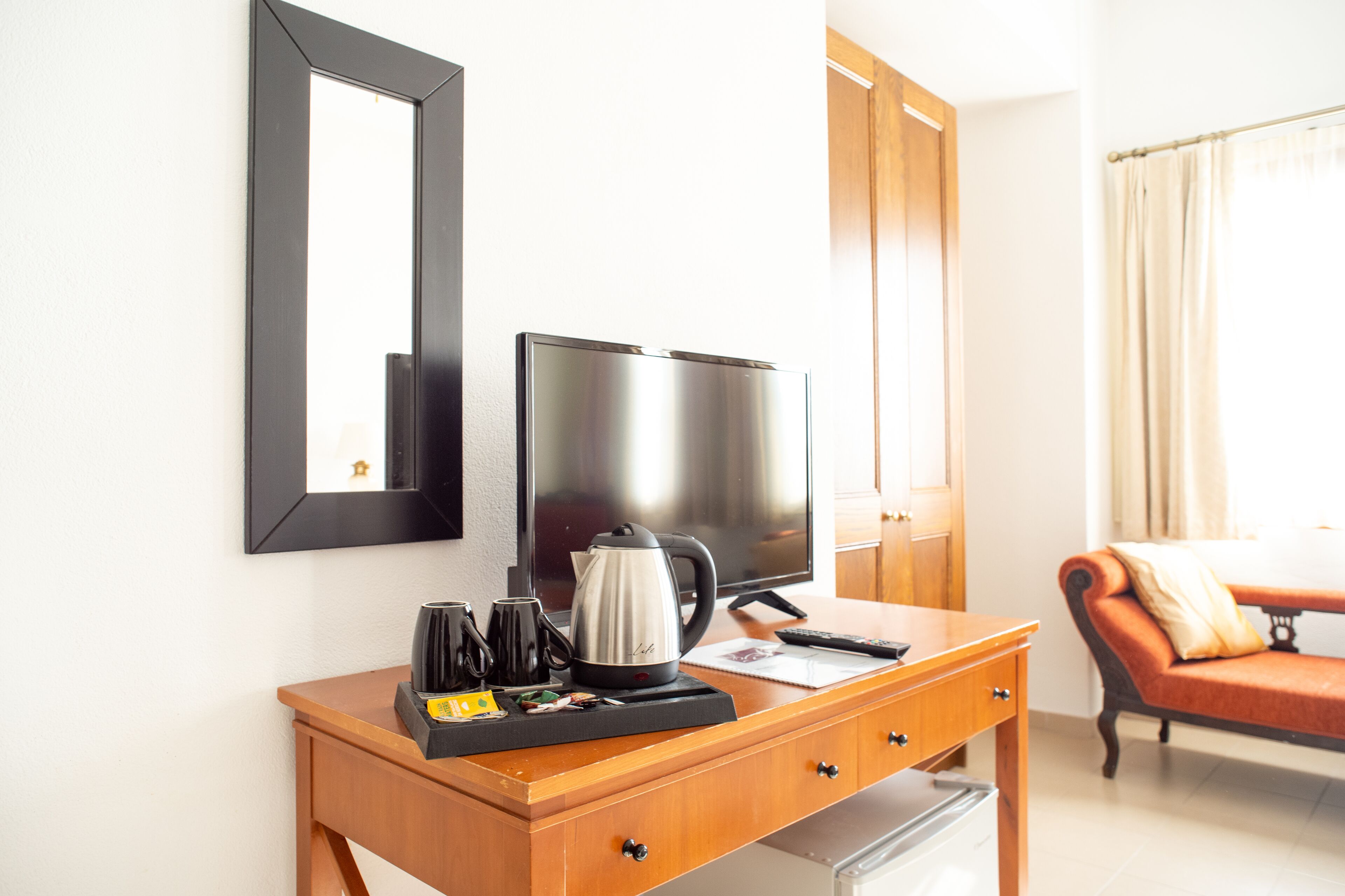Une chambre d’hôtel avec un bureau en bois, une télévision, une bouilloire et un canapé.