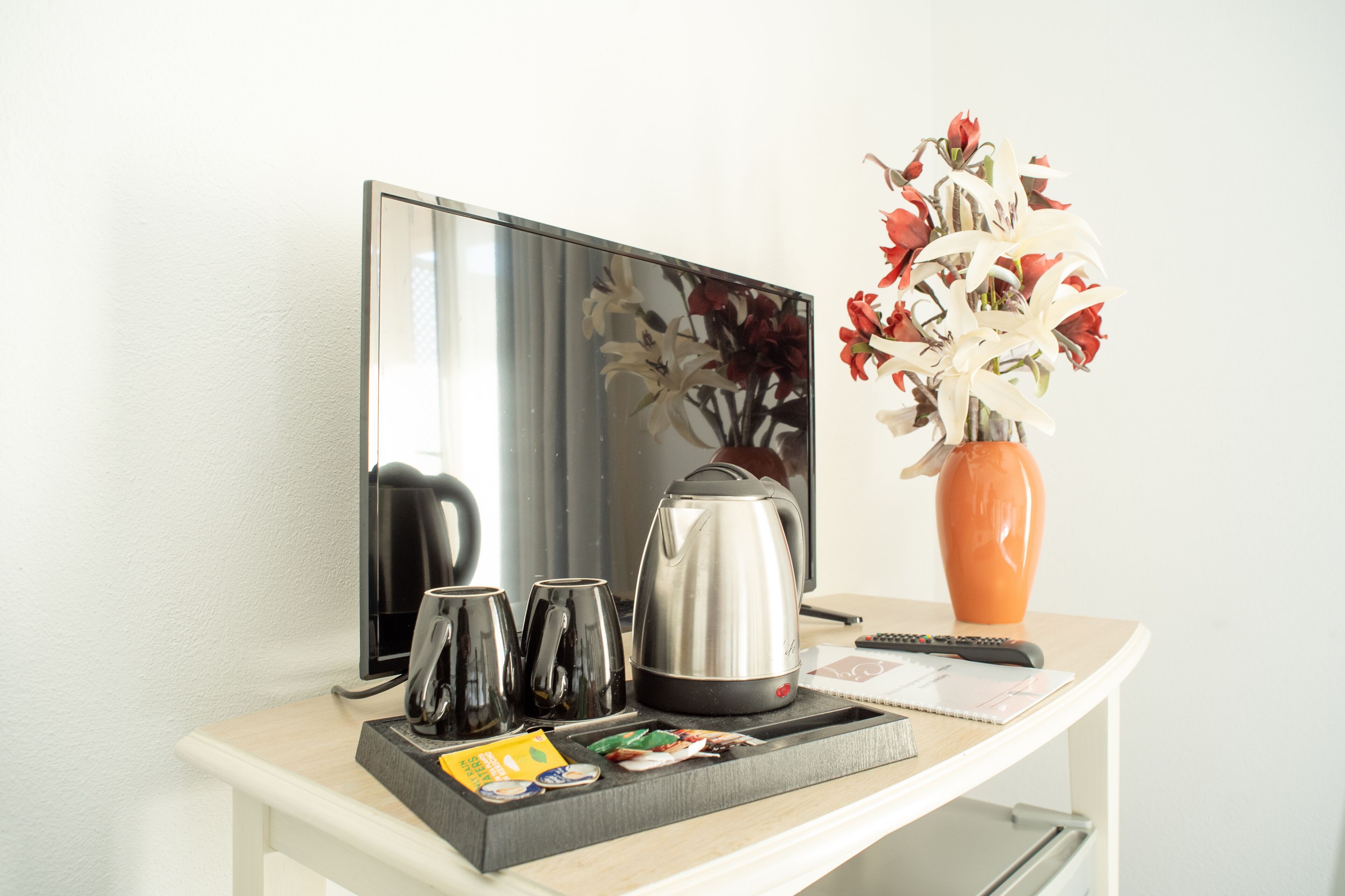 Une chambre d’hôtel équipée d’un téléviseur à écran plat, d’une machine à café, d’un vase avec des fleurs et d’un plateau contenant des tasses et des en-cas.