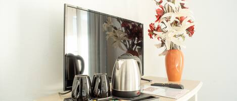 Quarto de hotel com televisão de tela plana, cafeteira, um vaso com flores e um tabuleiro com chávenas e petiscos.