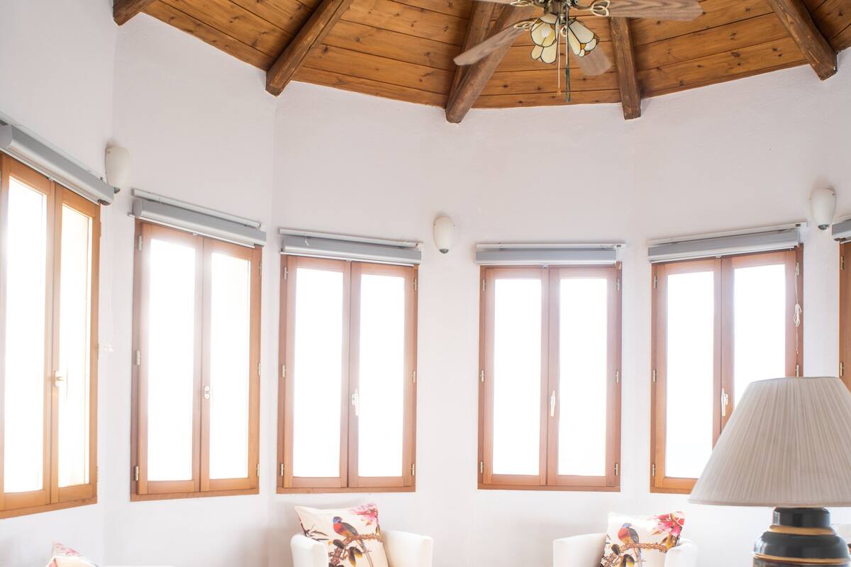 A spacious living room with wooden ceiling beams, large windows, and white furniture.
