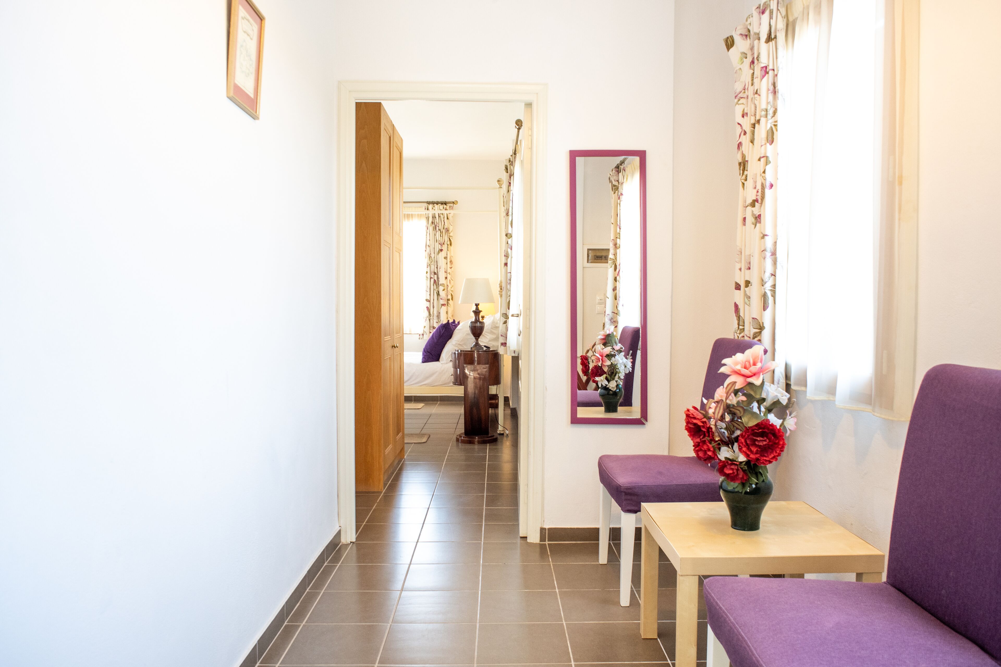 A hallway with a bed, a small table with a vase of flowers, and a purple chair.