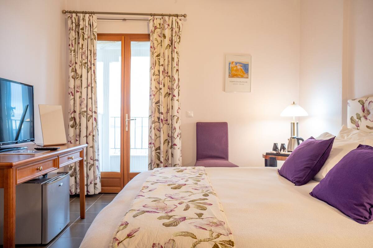 A hotel room with a bed, a desk with a computer, a chair, a lamp, and a small refrigerator.