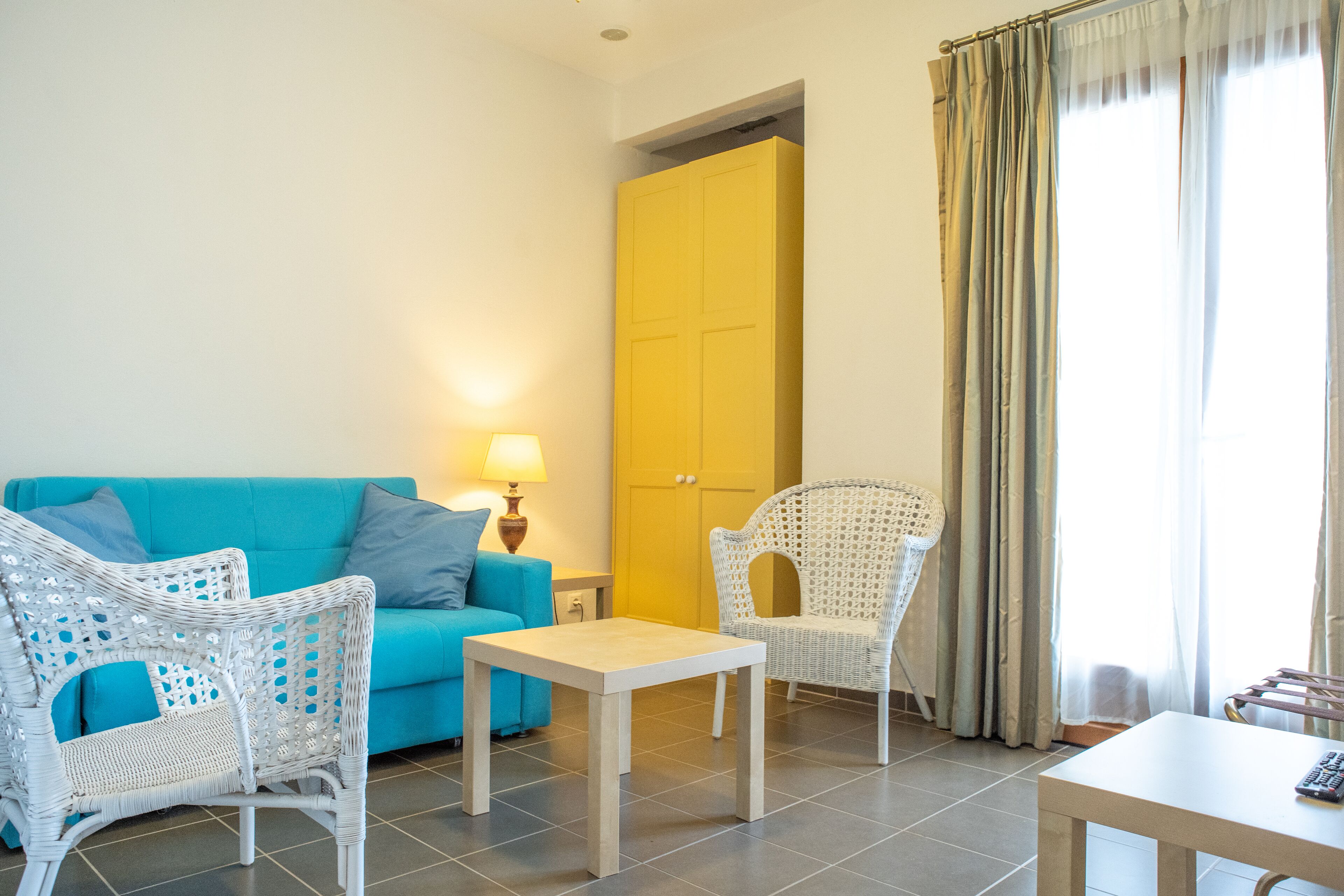 A room with a blue sofa, white wicker chairs, a small table, and a yellow door.