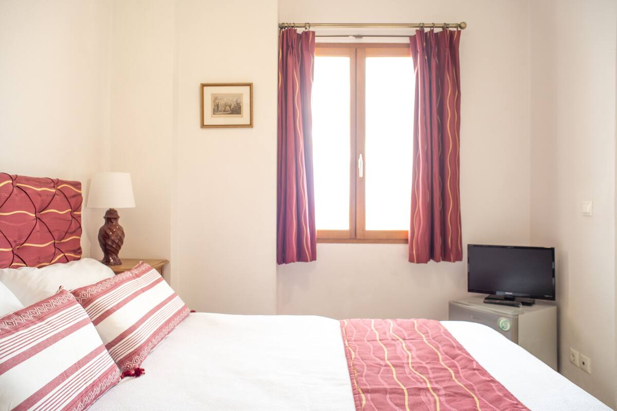 A hotel room with a bed, a television on a stand, and a window with curtains.
