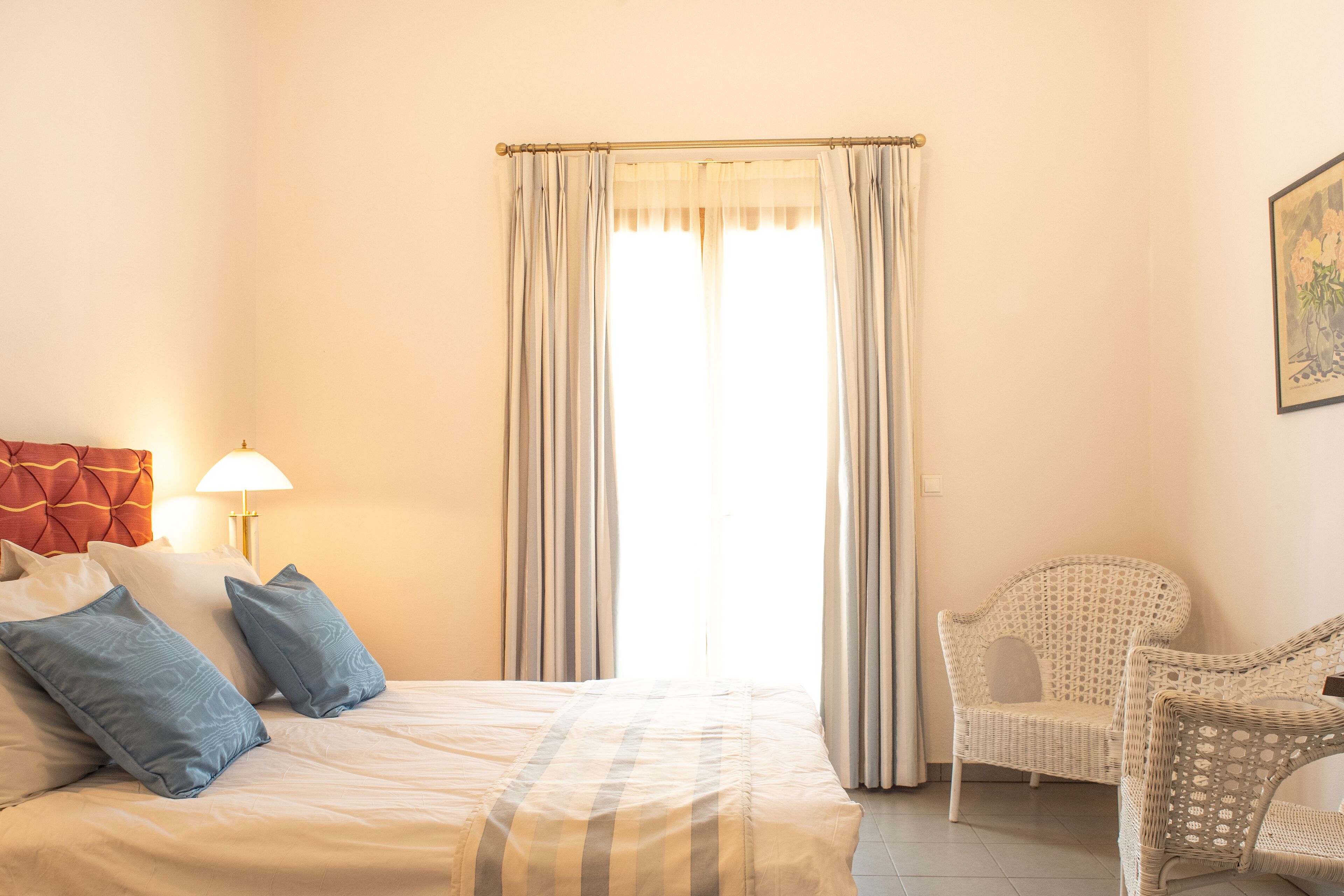 Ein Hotelzimmer mit einem Bett, Kissen, einem Sessel, einer Lampe und einem Fenster mit Vorhängen.