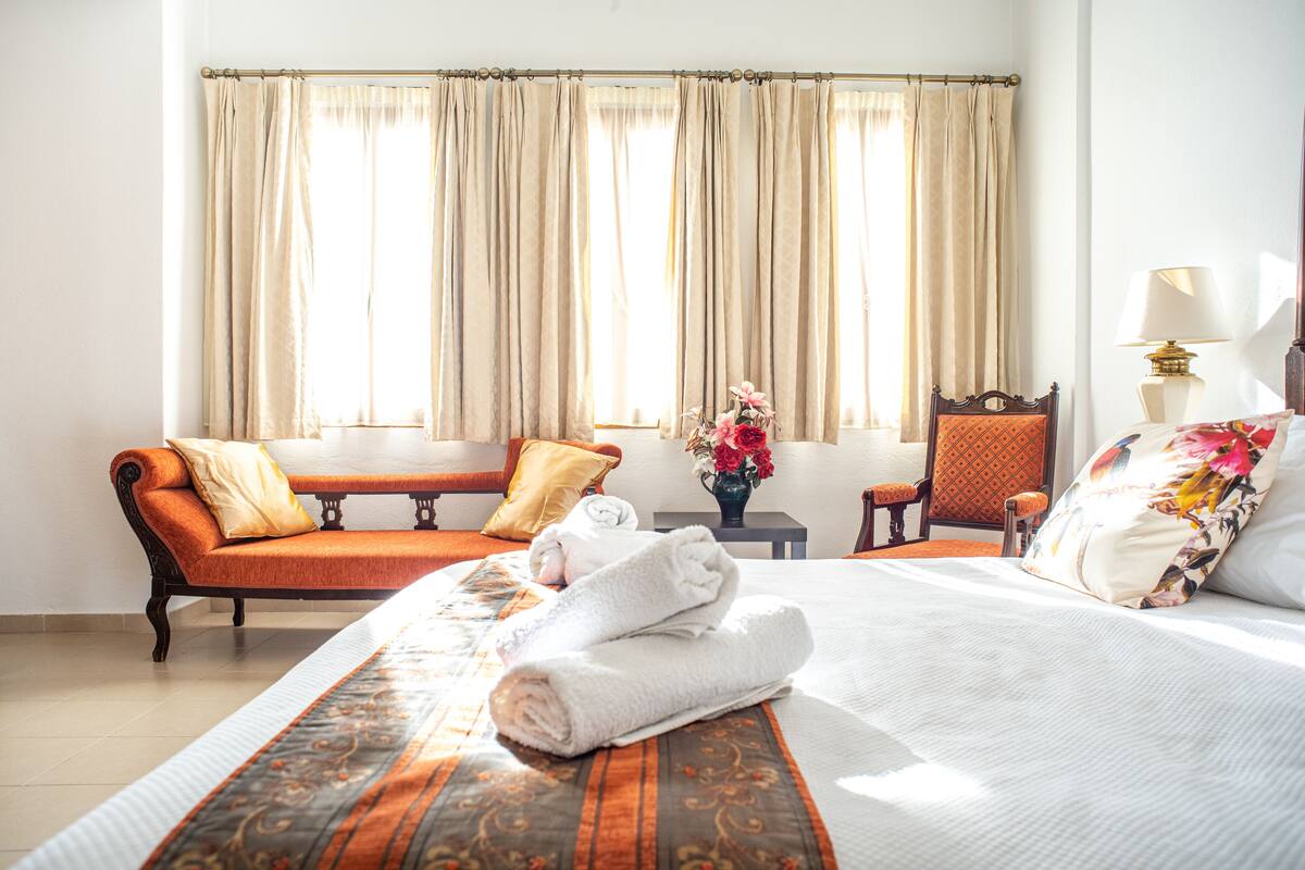 A hotel room with a bed, a sofa, a chair, a small table, and a lamp.