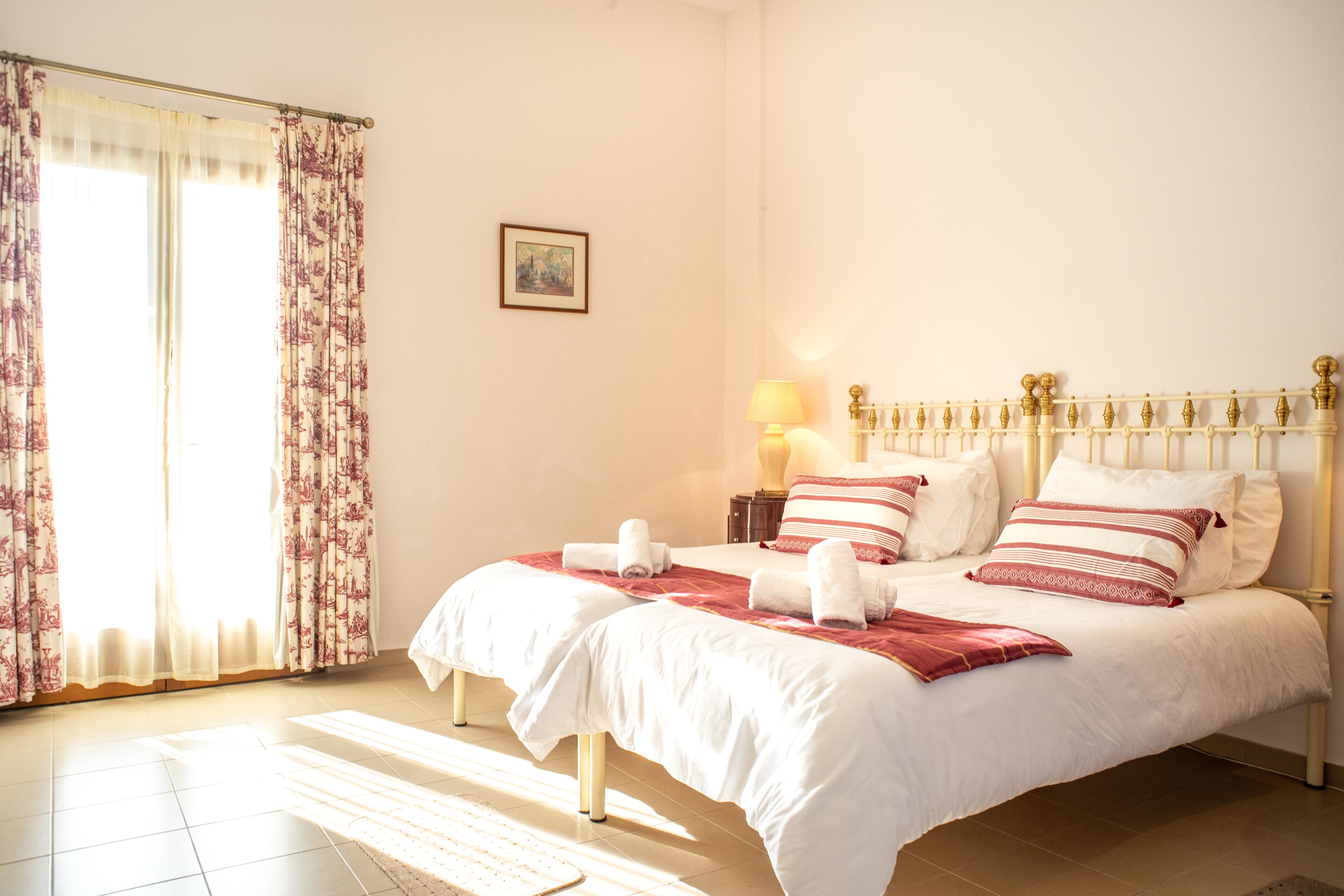 Un dormitorio con cama, cortinas, mesita de noche y lámpara.