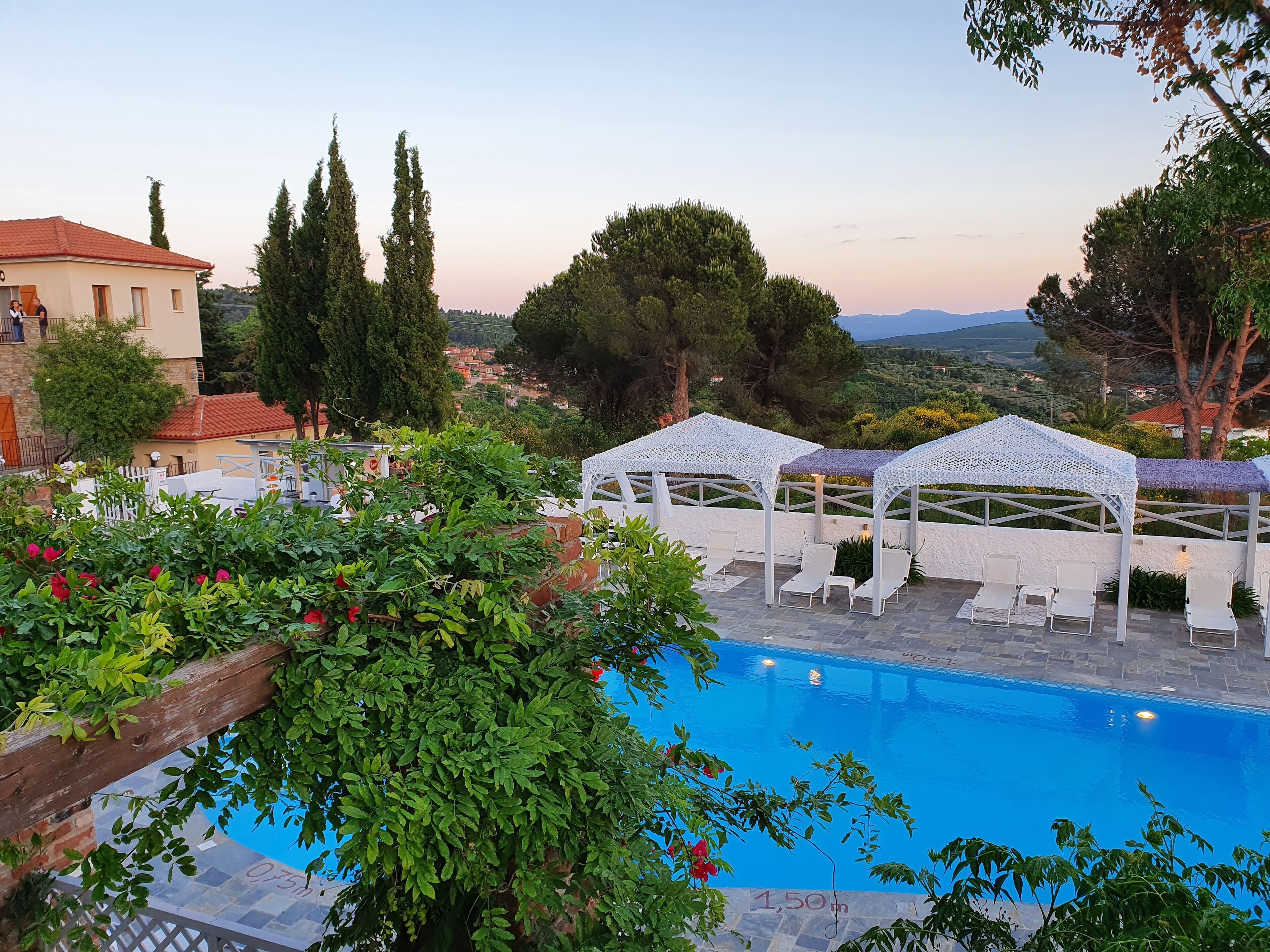 A pool area with white canopies and lounge chairs, surrounded by greenery and overlooking a scenic landscape.