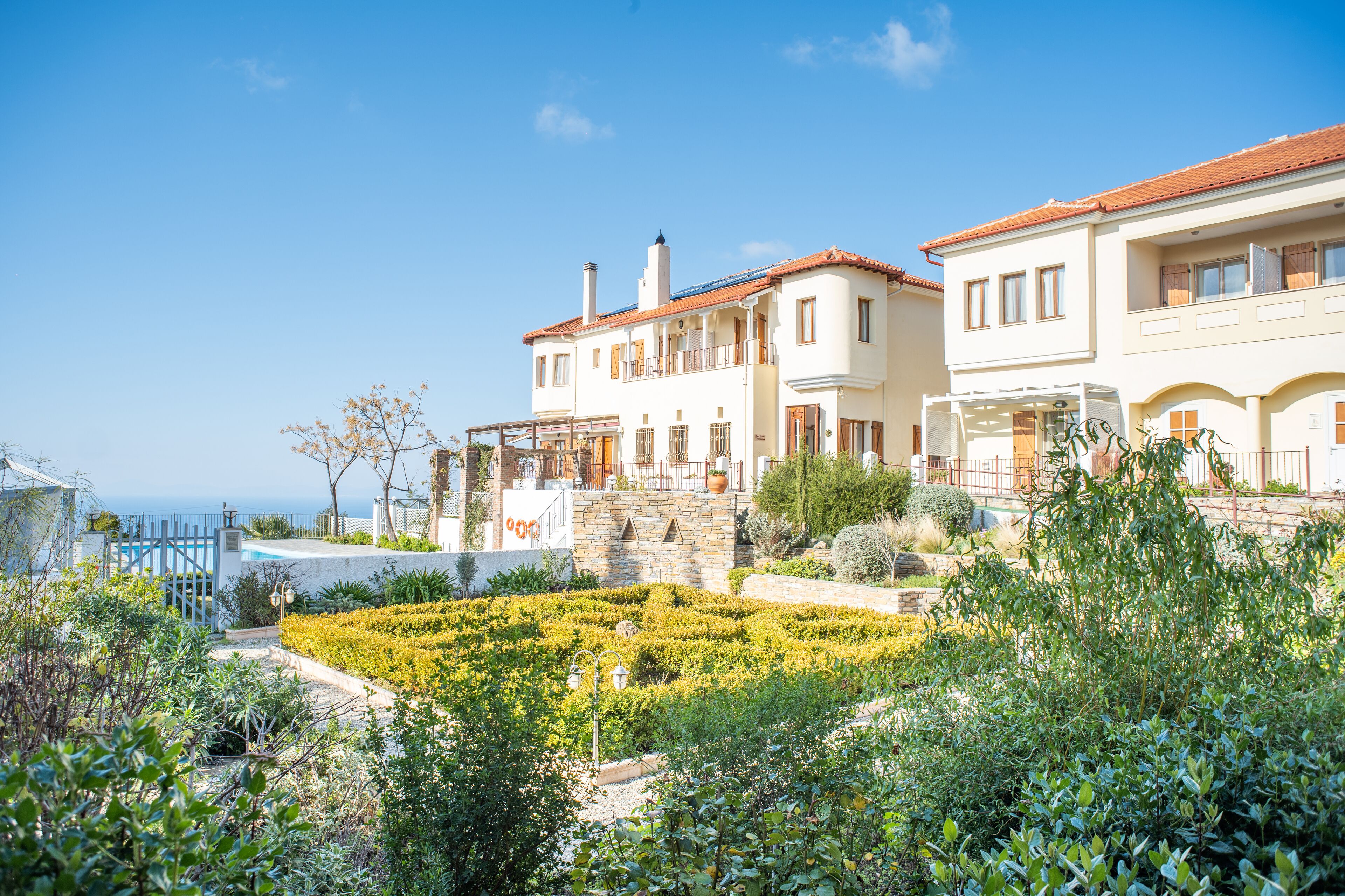 A two-story building with a garden in front, a pool, and a view of the sea.