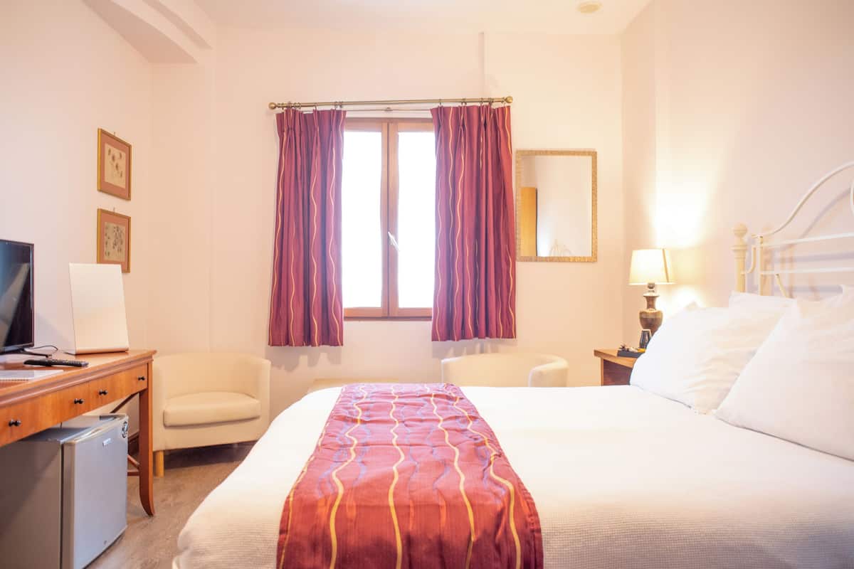A hotel room with a bed, a desk with a computer, a chair, a TV, and a window with curtains.