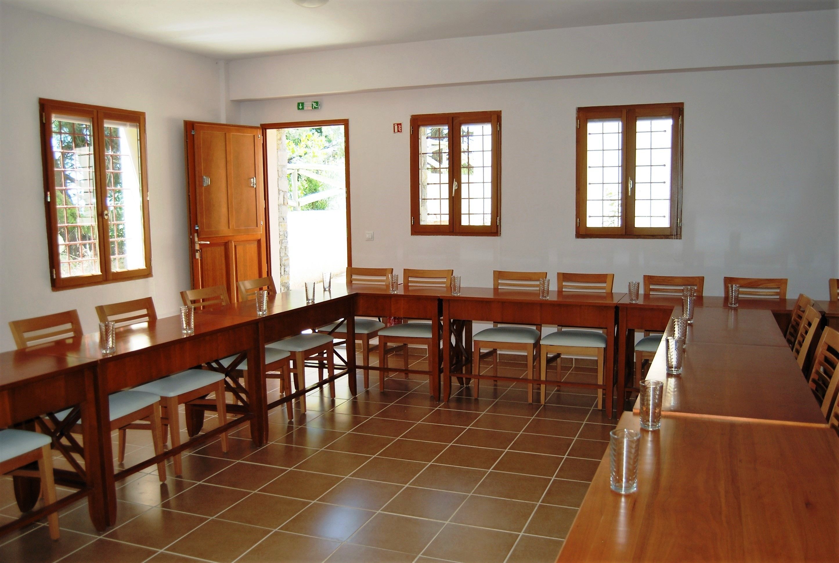 A conference room with a long wooden table, multiple chairs, and large windows with wooden frames.