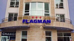 Un immeuble à plusieurs étages, reconnaissable à son grand panneau portant l’inscription « FLAGMAN », à ses larges fenêtres et à son balcon.
