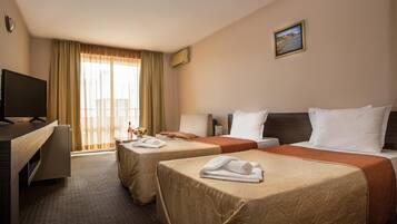 Ein Hotelzimmer mit zwei Betten, einem Schreibtisch, einem Fernseher und einem Fenster mit Vorhängen.