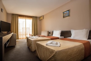 Habitación de hotel con dos camas, un escritorio, un televisor y una ventana con cortinas.