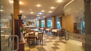 Un restaurante con mesas y sillas, un muro de cristal con texto, y un suelo a cuadros.
