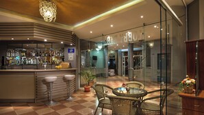 Un área de bar con taburetes, suelo de cuadros, mobiliario de mimbre y una pared de vidrio.