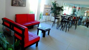 Een hotel lobby met een rode bank, een kleine tafel en een glazen scheiding tussen de zithoek en de bar.