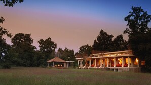 A large, modern house with a spacious porch and multiple rooms, surrounded by a grassy field and trees.