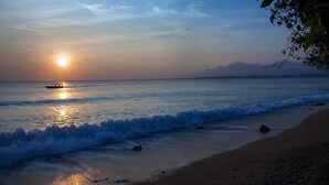 A beach scene with a boat on calm waters, a clear sky, and distant mountains. - Nusabay Menjangan by WHM (Sumberklampok)