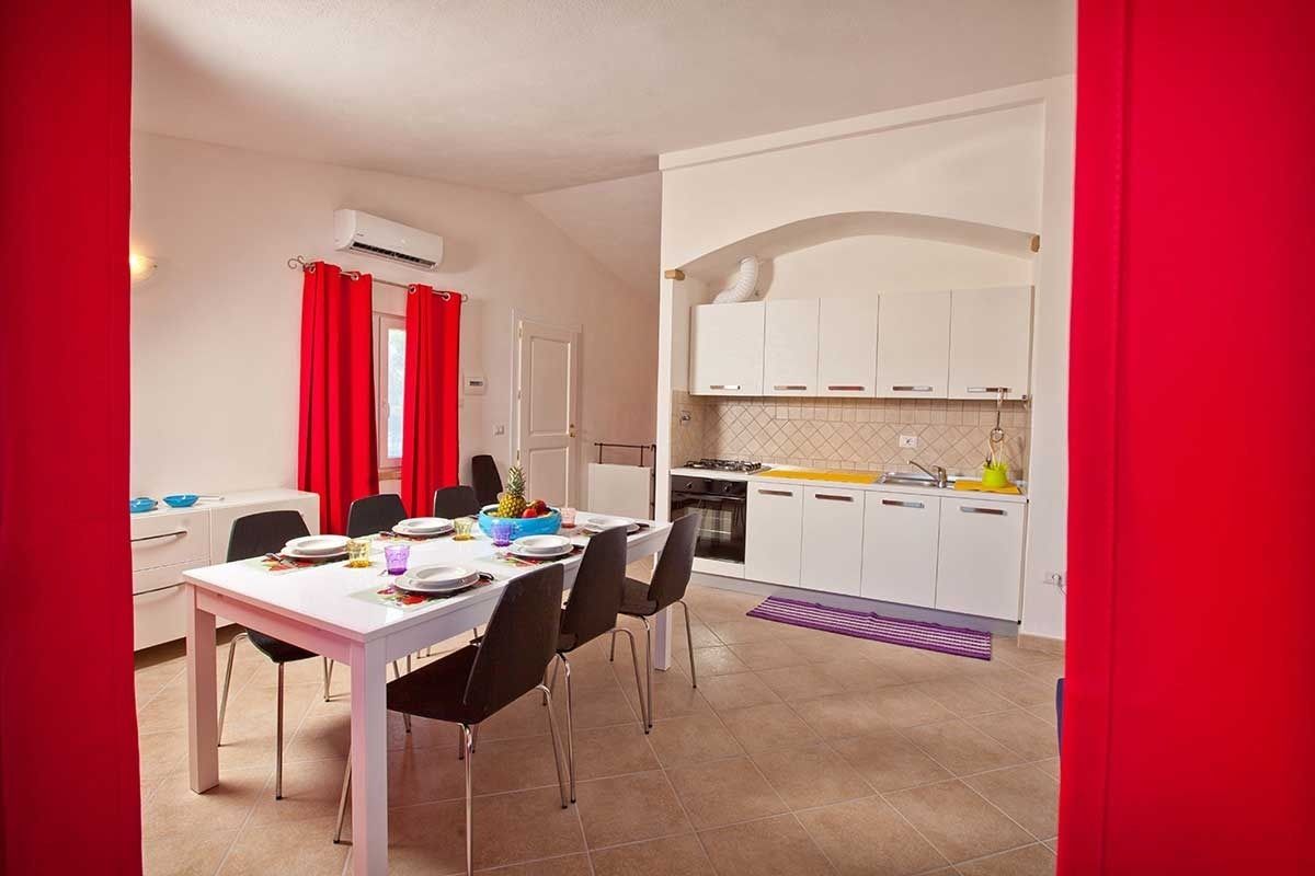 A compact kitchen with white cabinets, a dining area with a white table and black chairs, and red curtains.