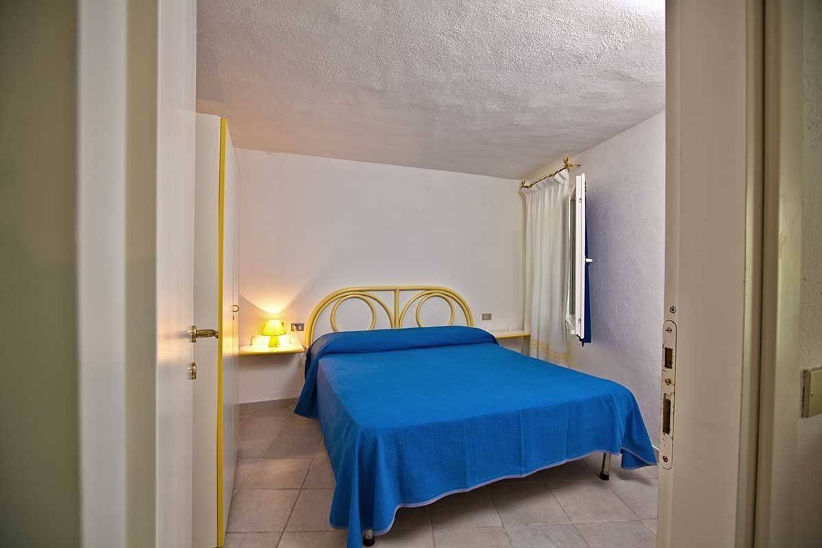 A bedroom with a bed, a bedside table with a lamp, and a window with curtains.