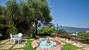 Un jardín con piscina, una fuente y una mesa con sillas.