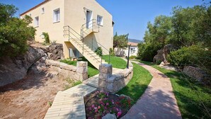 Un edificio de dos pisos con una escalera de piedra que conduce a la entrada, rodeado de un jardín ajardinado con un sendero.