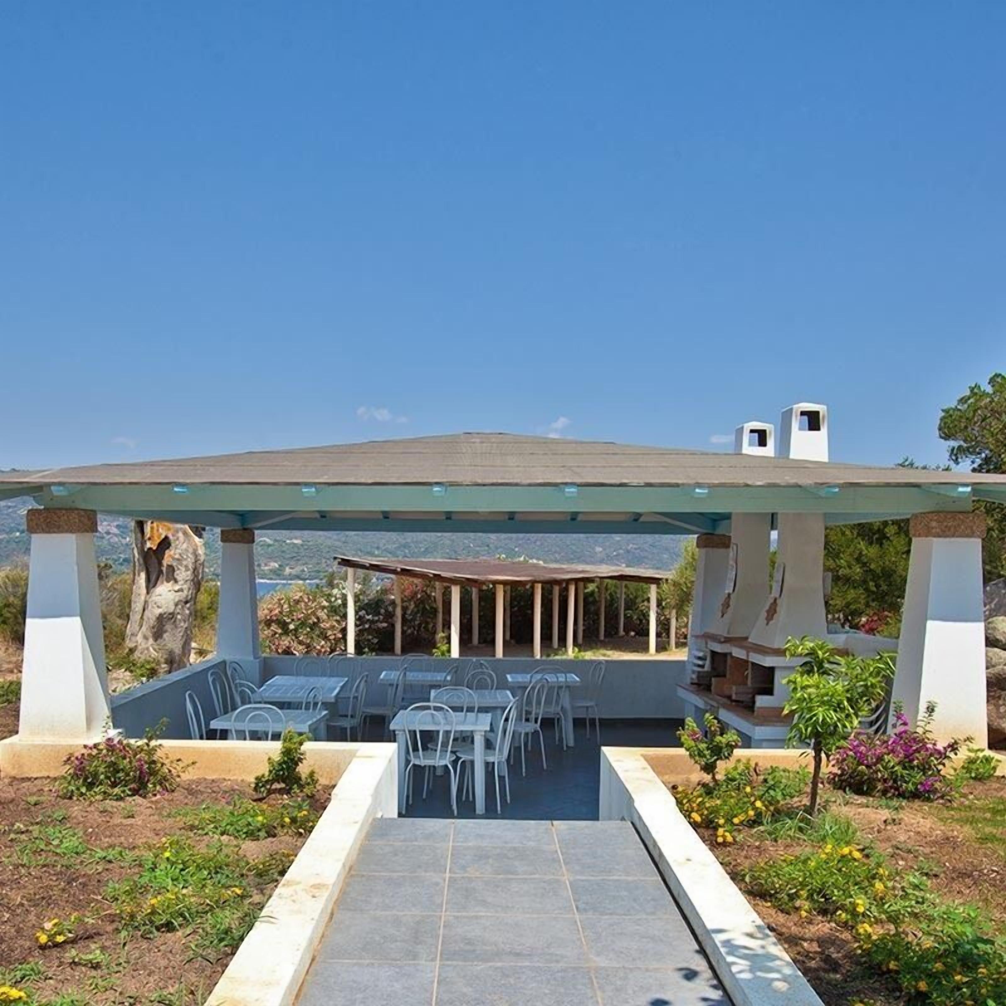 An outdoor patio with a covered seating area, a barbecue grill, and a view of the landscape.