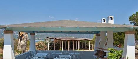 An outdoor patio with a covered seating area, a barbecue grill, and a view of the landscape.